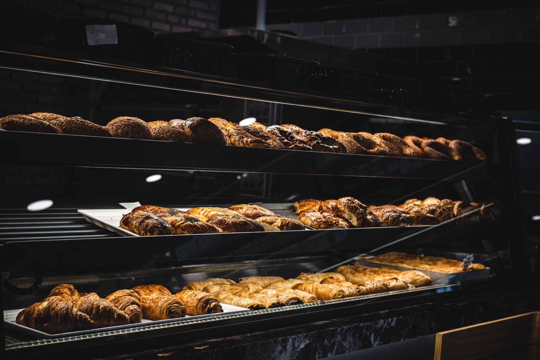 Vitrină de patiserie cu croissante și plăcinte pe trei rafturi de sticlă, fără clienți în cadru.
